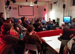 people sitting in an event space, watching a screen